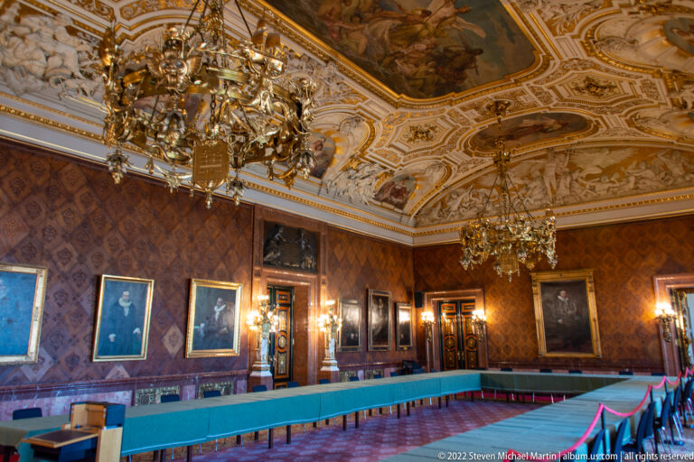 Ornate Hamburg Rathaus state room with long U-shaped table, portraits, gilded chandeliers, and painted ceiling.