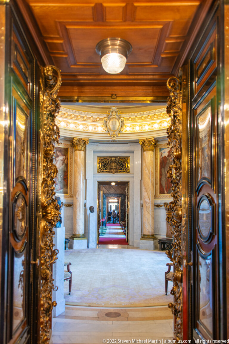 Ornate carved doorways form a long enfilade through ceremonial rooms of Hamburg Rathaus, with gilding and red carpet beyond.