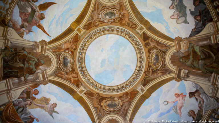 Circular painted ceiling with allegorical figures, gilded ribs, and a pale sky-filled oval at the center.
