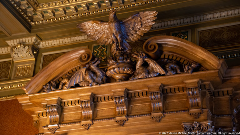 Carved wooden eagle with spread wings above dense scrollwork and animal ornament on a ceremonial overdoor.