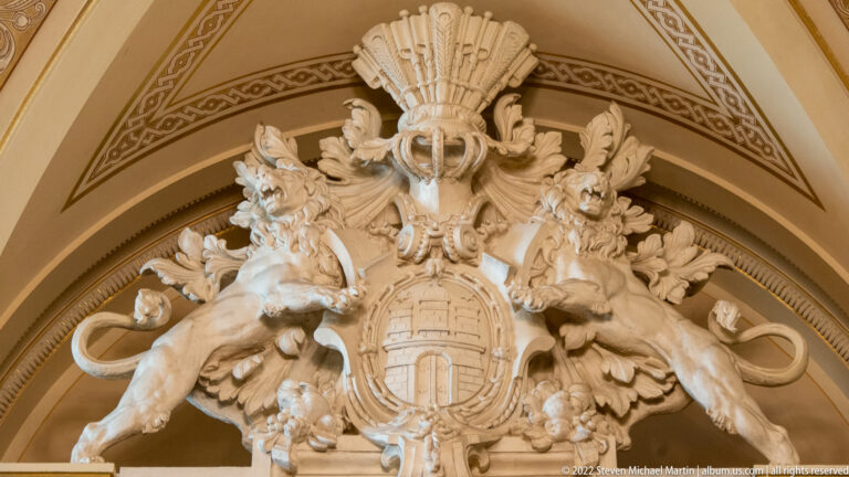 Pale stone Hamburg coat of arms with two rampant lions beneath a shell-like crest in an arched interior panel.