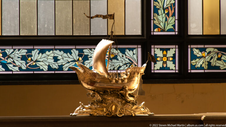 Decorative metal sailing ship with illuminated sail displayed beneath floral stained-glass panels.