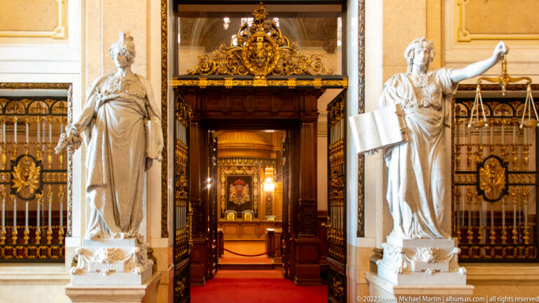 Ornate dark-wood Rathaus doorway between two pale stone allegorical women, with Justice holding scales at right.
