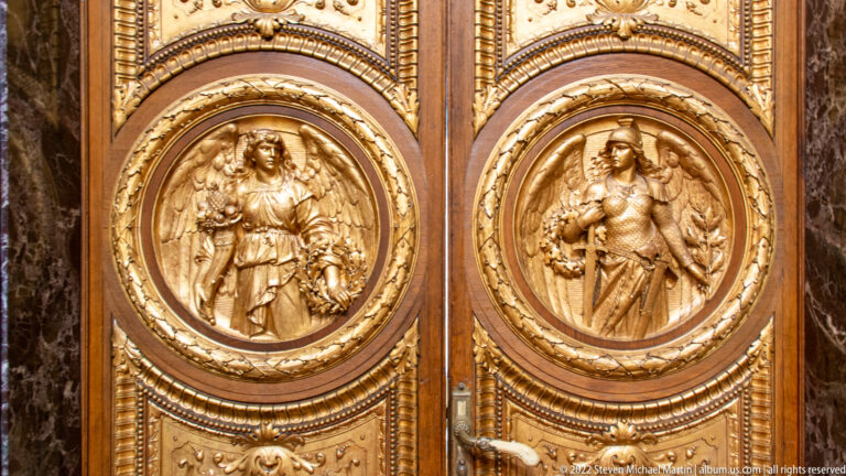 Pair of ornate wooden doors with circular gilded reliefs of standing female figures and concentric carved borders.