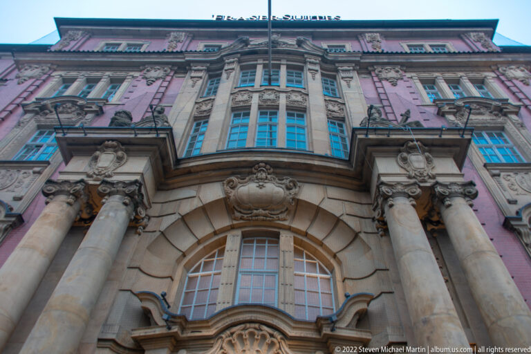 Upward view of ornate pink and pale-stone historic façade with columns, cartouches, and arched windows.
