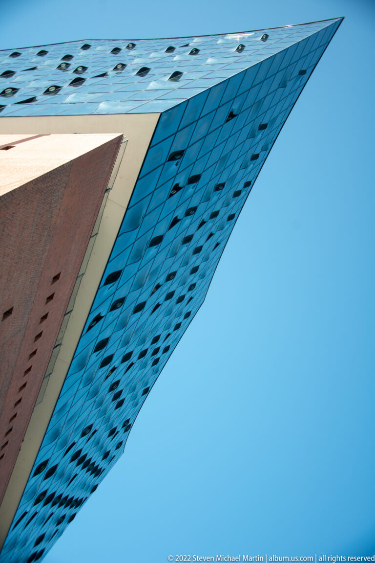 Sharp overhanging corner of the Elbphilharmonie glass façade viewed from below against blue sky.