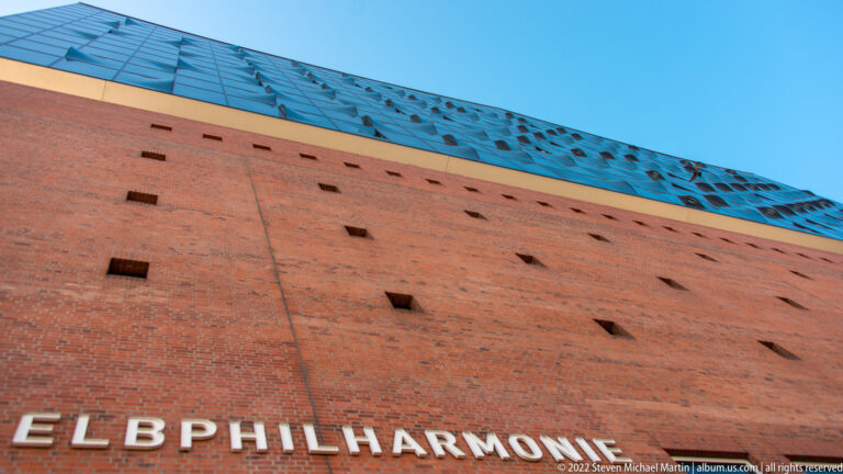 Red-brick base of the Elbphilharmonie with white building name and blue glass superstructure above.