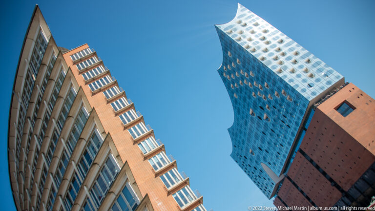 Elbphilharmonie glass tower rising above a neighboring brick-and-glass building in a steep upward view.