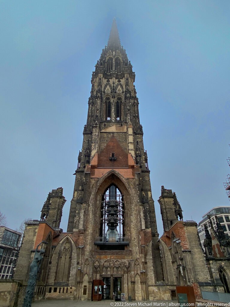 Frontal view of St. Nikolai Memorial with tall Gothic tower above roofless ruined church walls and exposed window openings.