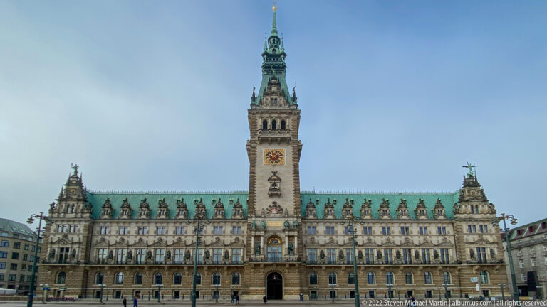 Full frontal view of Hamburg Rathaus with tall central clock tower, long ornate façade, and green copper roof.