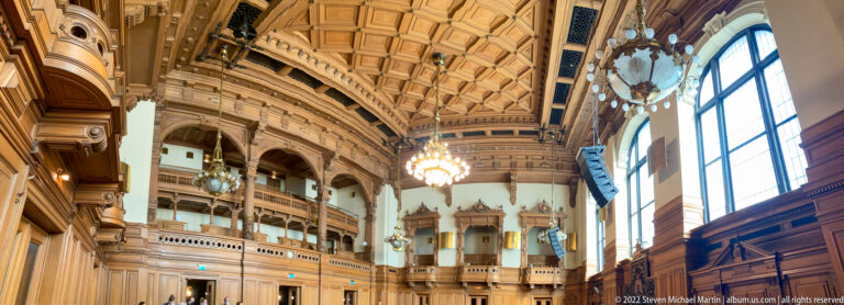 Grand Hamburg Rathaus hall with dark wood paneling, tall windows, chandeliers, galleries, and a richly coffered ceiling.