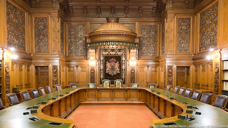 U-shaped council table with leather chairs beneath carved wood paneling and Hamburg’s coat of arms.