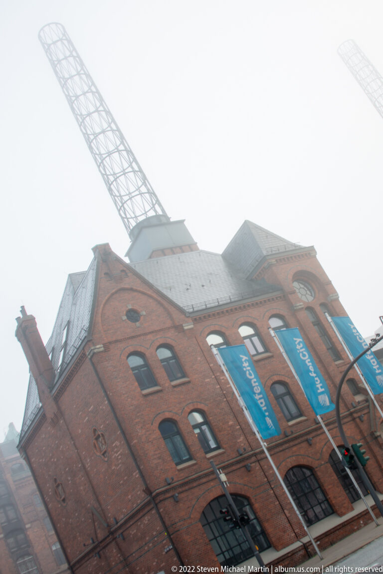 Red-brick harbor building with tall arched windows and blue banners beneath a large lattice-boom crane.