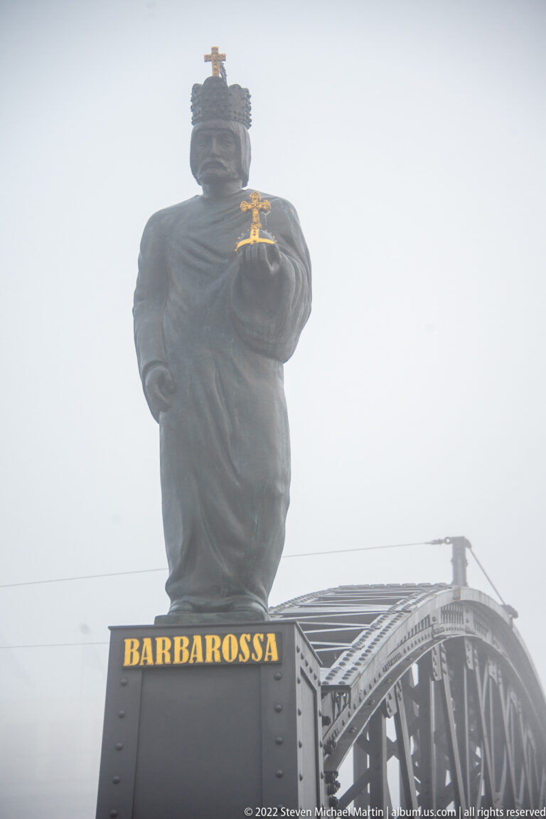 Statue of Barbarossa above a steel bridge, holding a gilded object in dense Hamburg fog.