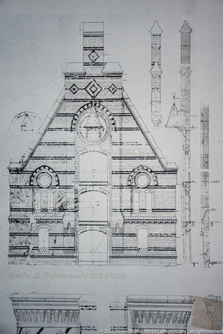 Historic elevation drawing of an ornate gabled façade with central arch, round windows, and small roof-detail studies.