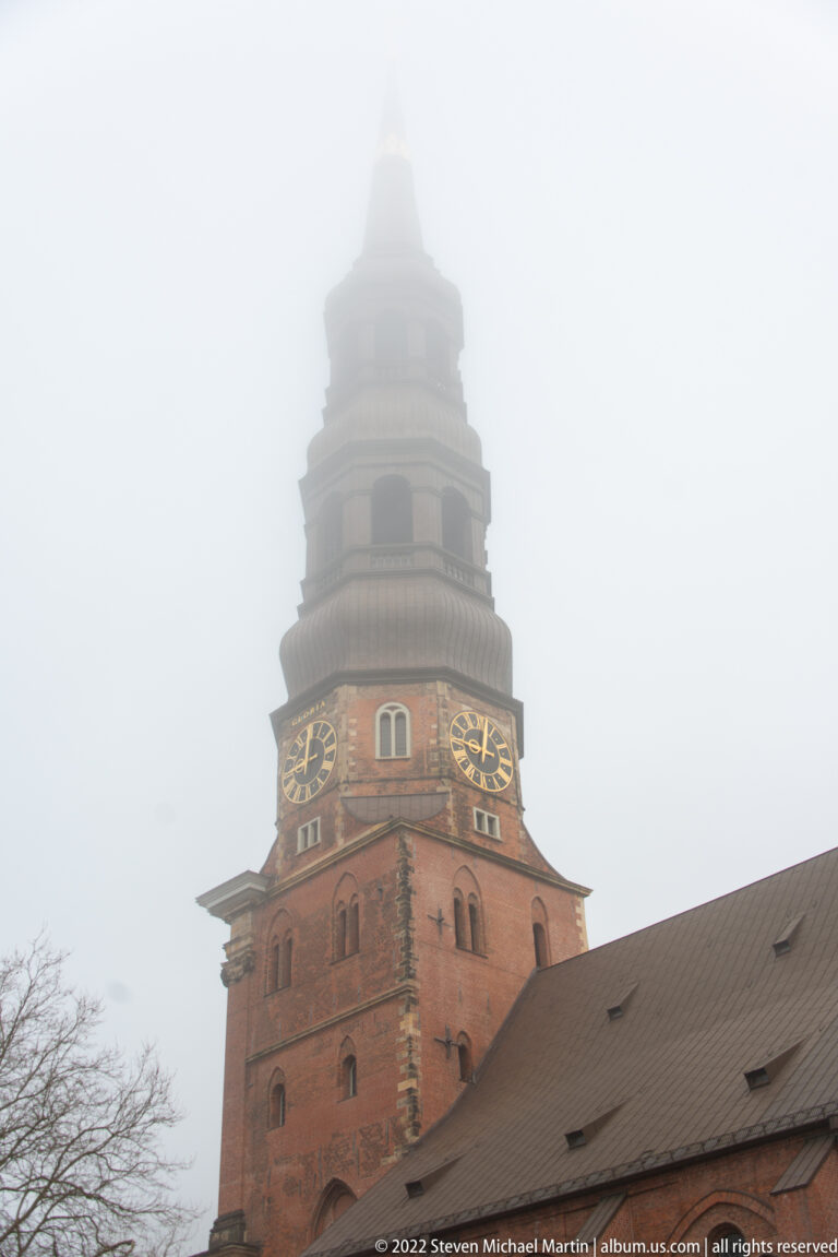 Brick tower of St. Catherine’s Church with twin clock faces rising into dense fog above the church roof.