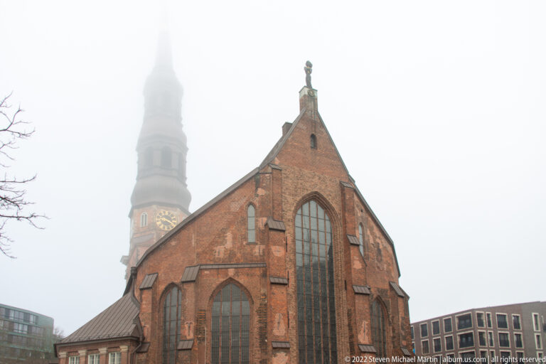 Brick Gothic east end of St. Catherine’s Church with tall pointed windows and its foggy tower behind.