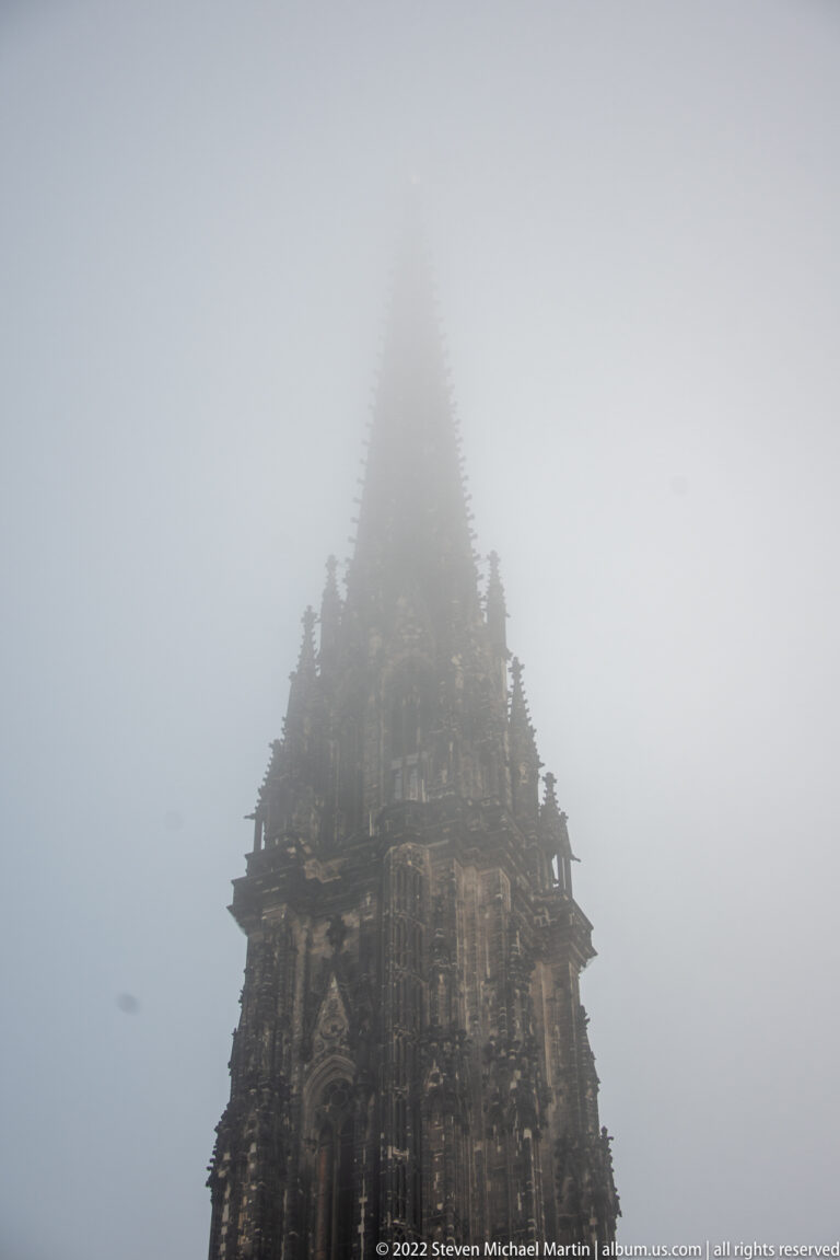 Dark Gothic tower of St. Nikolai Memorial rising into dense fog, with the upper spire disappearing from view.