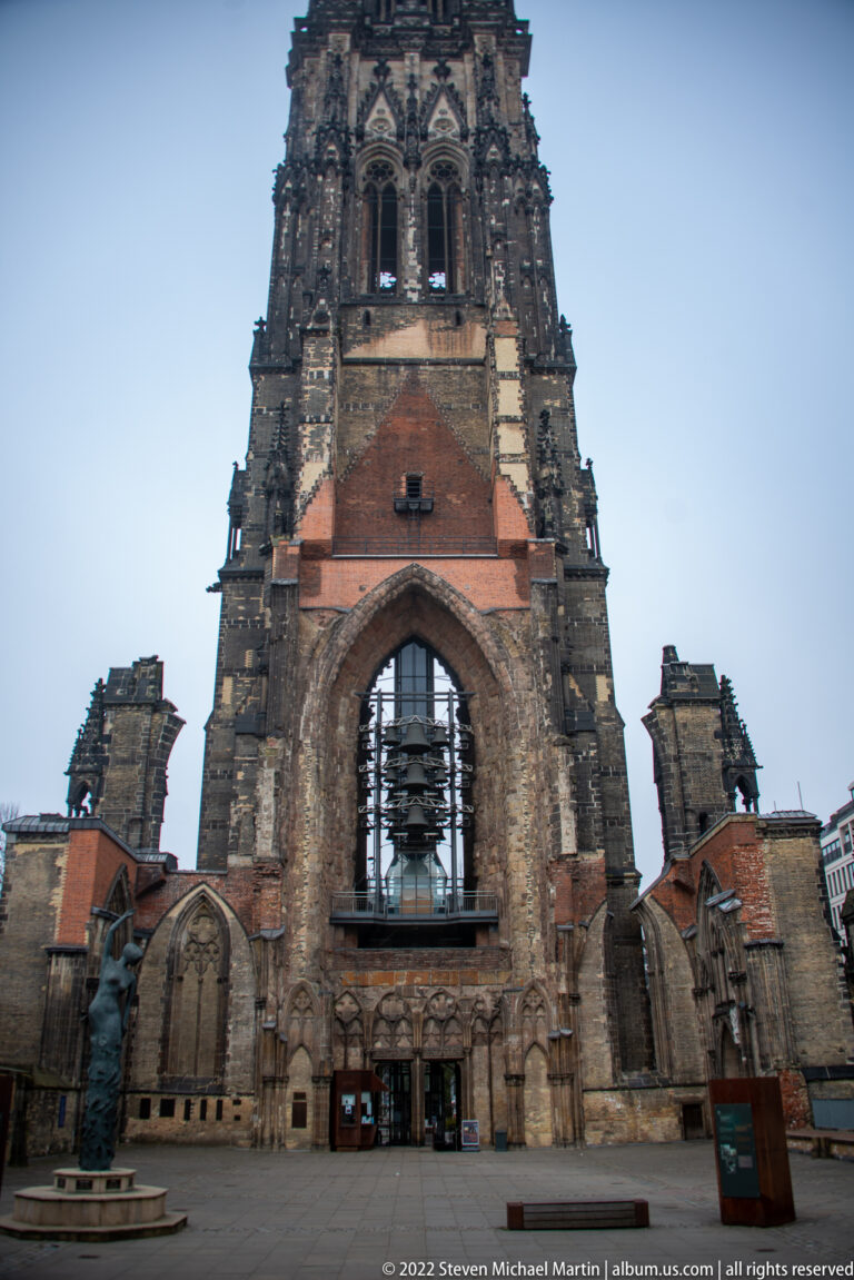 Frontal view of St. Nikolai’s ruined west façade, with a large pointed arch, exposed bells, and roofless side walls.