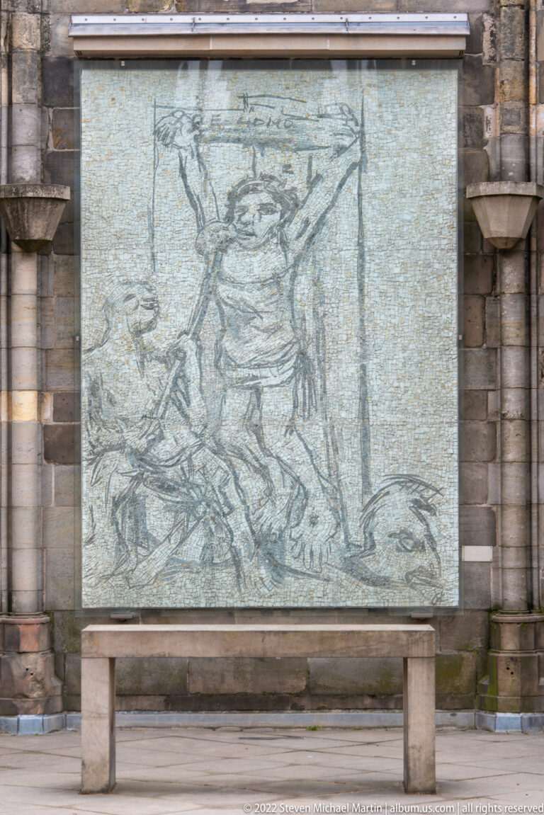 Large pale monochrome memorial panel with a sketch-like human figure mounted against dark stone masonry.