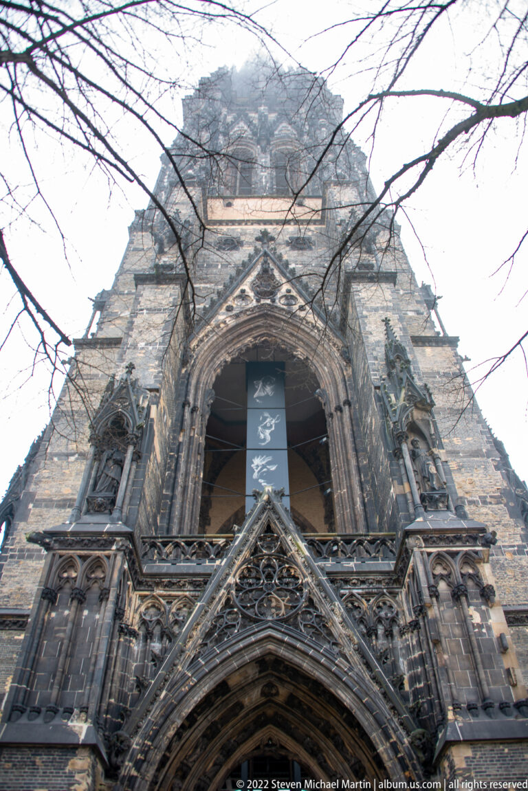 Steep upward view of an ornate Gothic portal with pointed arches, tracery, niches, and weathered stonework.