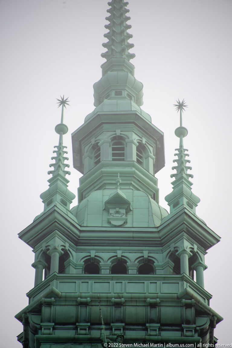 Close view of Hamburg Rathaus’s green copper upper tower with arcaded openings, corner turrets, and star-like finials.