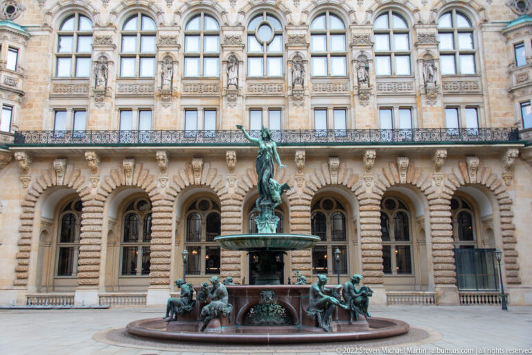 Full Hygieia Fountain before the rusticated arcade and upper windows of the Hamburg Rathaus courtyard.