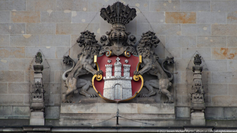 Hamburg coat of arms with red castle shield supported by two sculpted lions on the Rathaus façade.