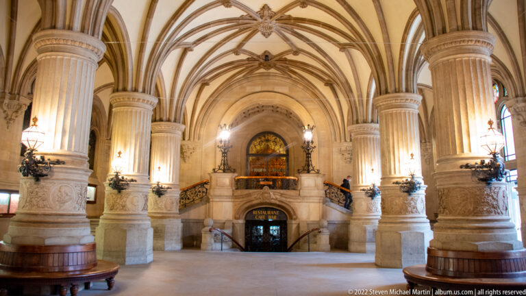 Grand Hamburg Rathaus hall with ribbed vaults, stone columns, ornamental lamps, and a central staircase.