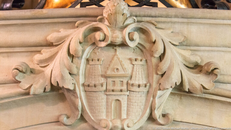 Carved stone Hamburg castle emblem within a scrolling foliate cartouche on the Rathaus interior.
