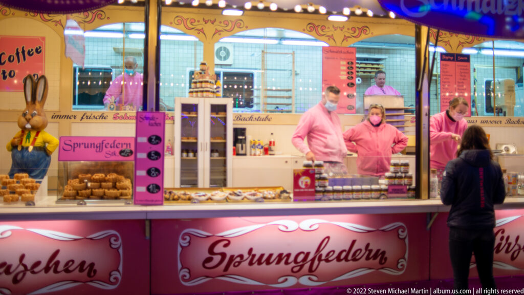 Pink Sprungfedern food stall with two staff members behind the counter, baked goods, jars, and a customer in front.