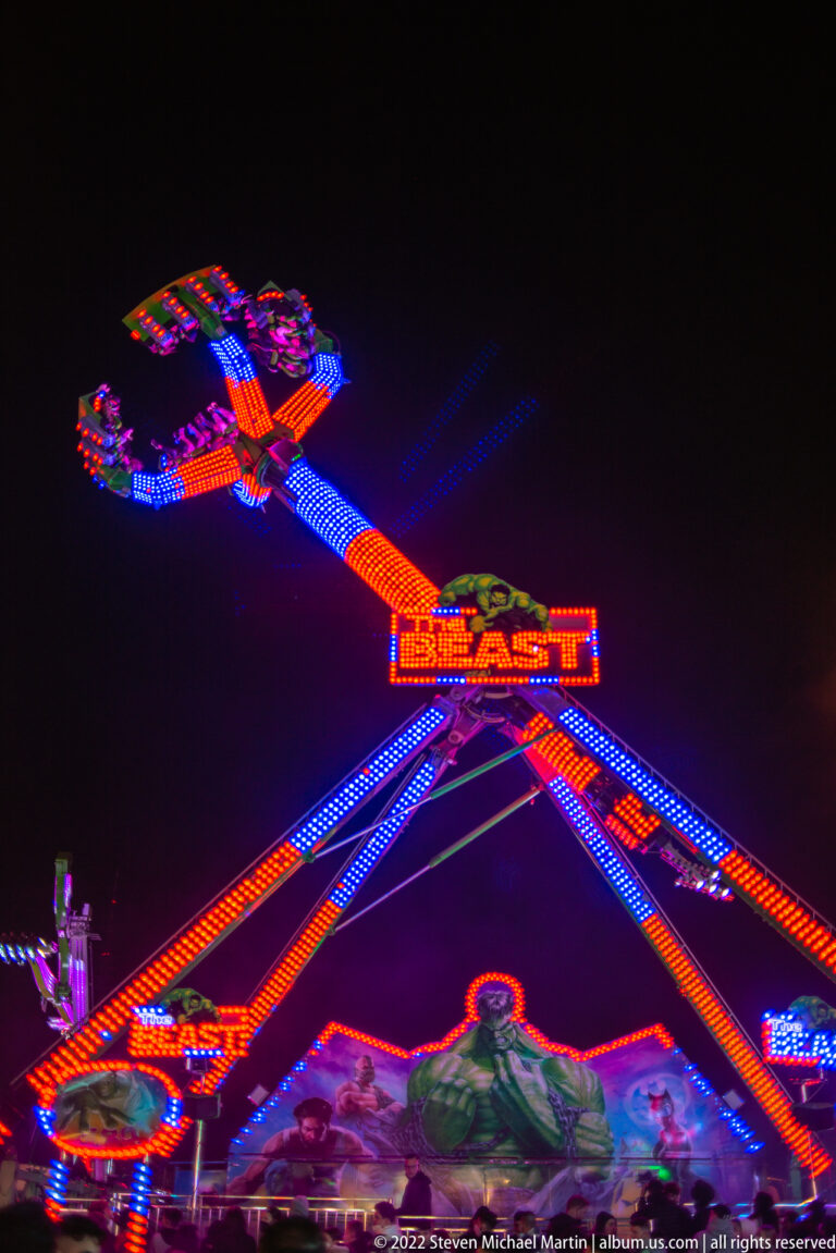 Large fairground thrill ride with red, blue, and purple illuminated arms blurred in motion against the night sky.