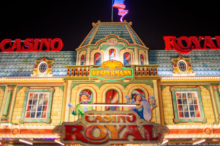 Ornate illuminated Casino Royal fairground façade with red lettering, painted figures, faux windows, and a central pediment.