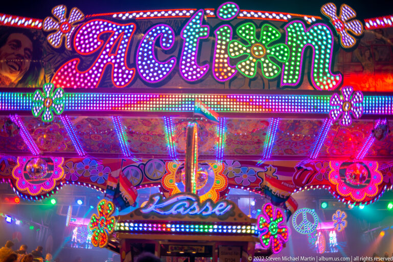 Brightly illuminated Action attraction entrance with multicolored LEDs, flower motifs, and reflective decorative panels.