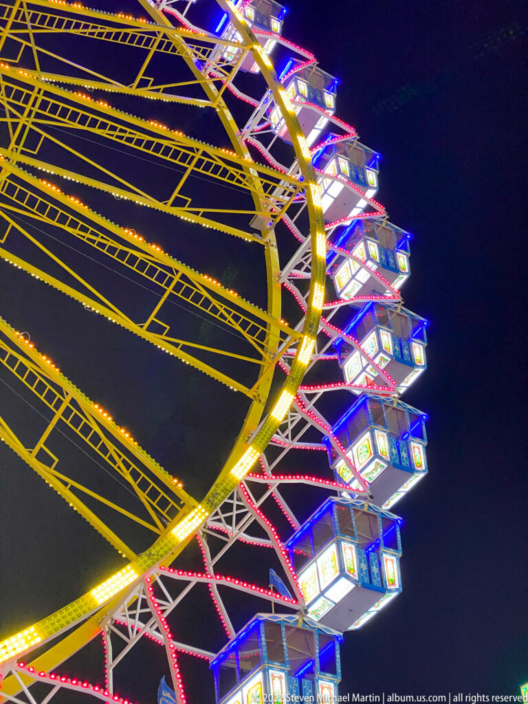 Close upward view of Ferris wheel gondolas and brightly lit metal lattice against the night sky.