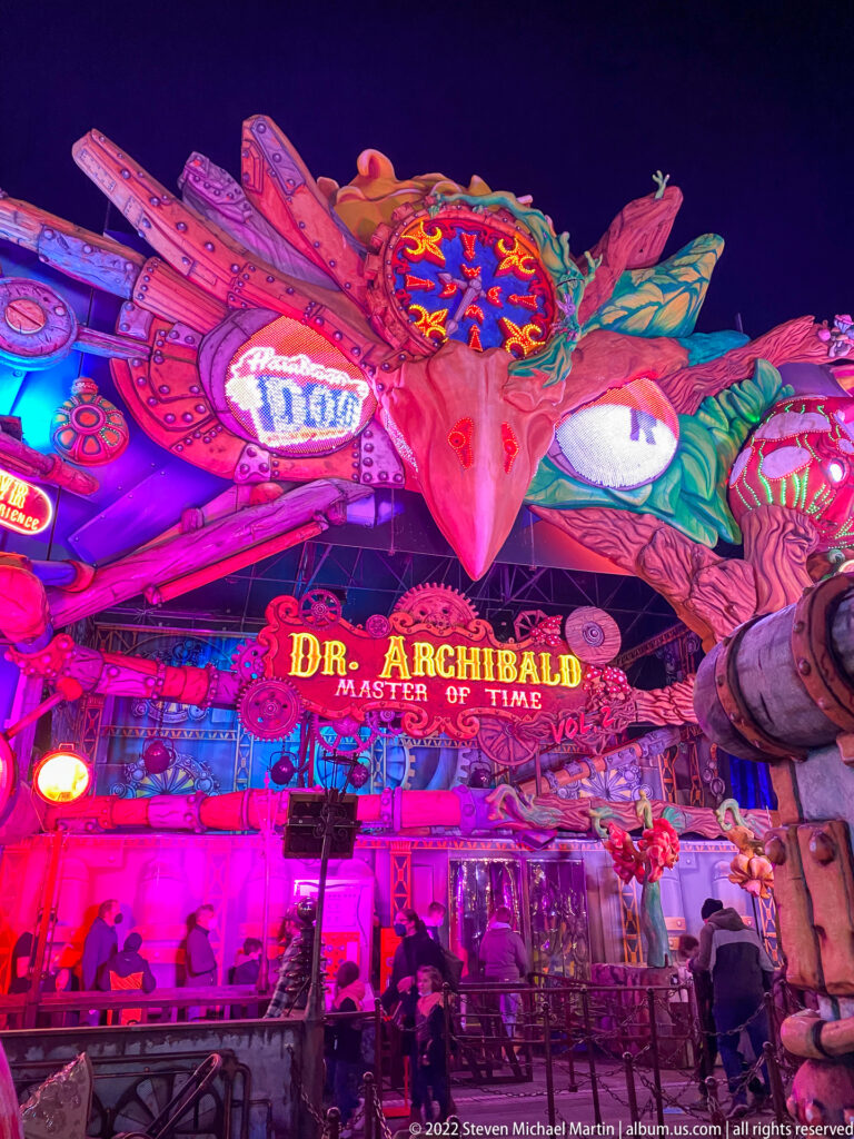 Dr. Archibald Master of Time façade glowing in magenta and blue, with visitors at the entrance below.