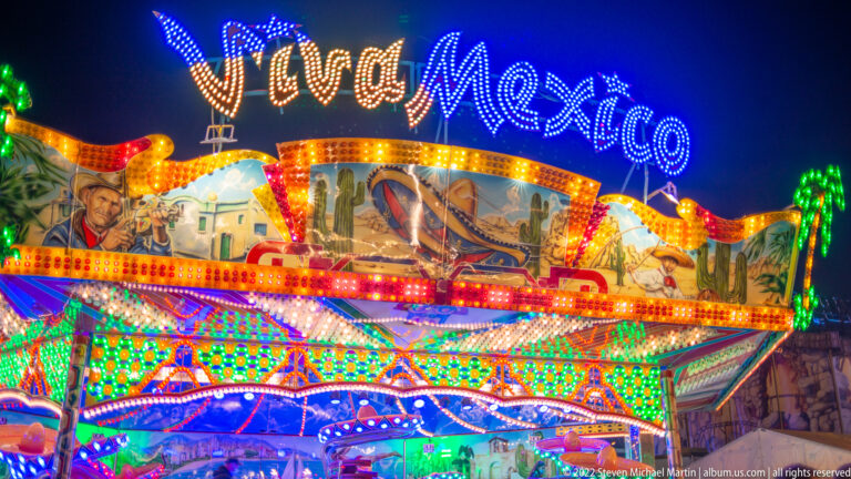 Colorful World Mexico fairground façade covered with multicolored lights and painted themed panels at night.