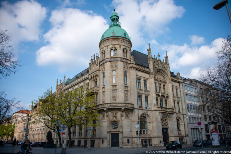 Ornate historic corner building with rounded bay, green copper dome, tracery, and sculptural stone façade.