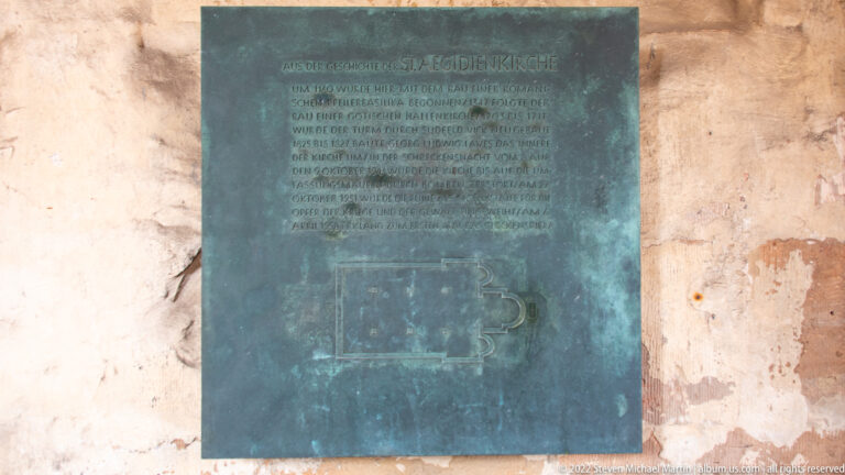 Green-patinated bronze plaque with German text and a plan diagram mounted on a wall inside Aegidienkirche.