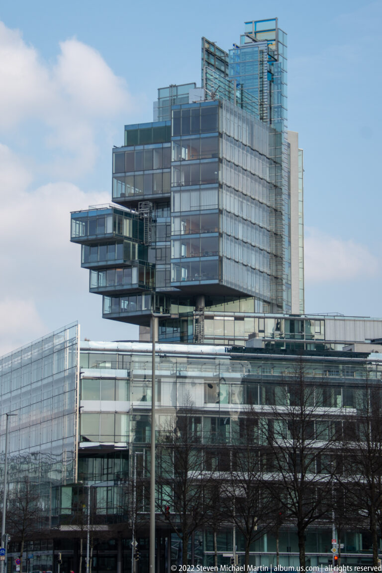 Modern glass-and-steel office complex with stacked cantilevered volumes above a broad glazed base.