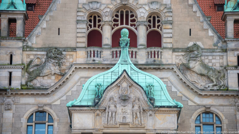Façade detail of the Neues Rathaus with arched windows, large stone beasts, balustrade, and a small copper roof.