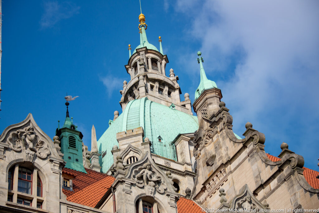 Upward view of the Neues Rathaus roofline with green copper domes, gilded finial, turrets, and carved gables.