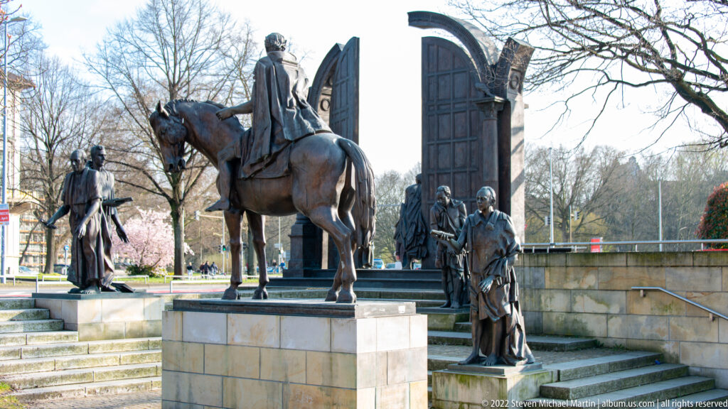 Bronze equestrian monument on a stone pedestal with several standing figures arranged around it.
