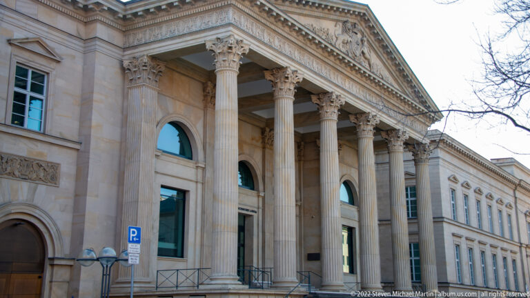 Stone civic building with tall classical columns, arched openings, carved entablature, and triangular pediment.