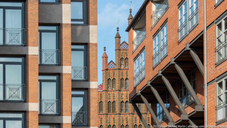 Decorative red-brick Gothic tower seen between modern and historic buildings in central Hannover.