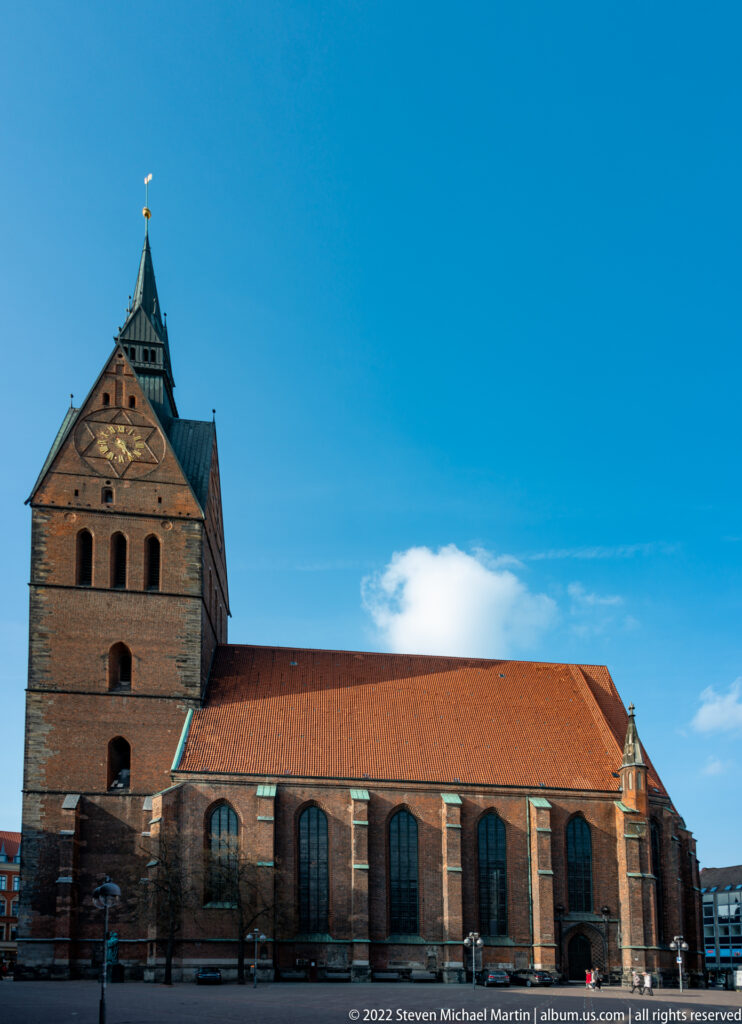 Large brick church with square west tower, red-tiled nave roof, and tall pointed-arch windows.