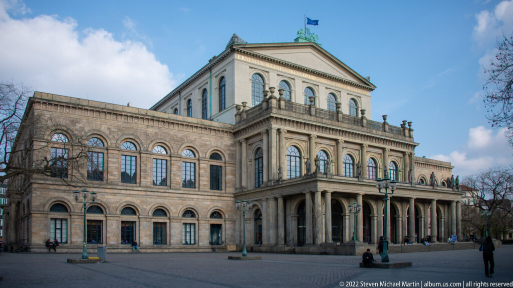 Oblique view of the pale stone Staatsoper Hannover with arcaded ground floor, arched windows, and central pediment.