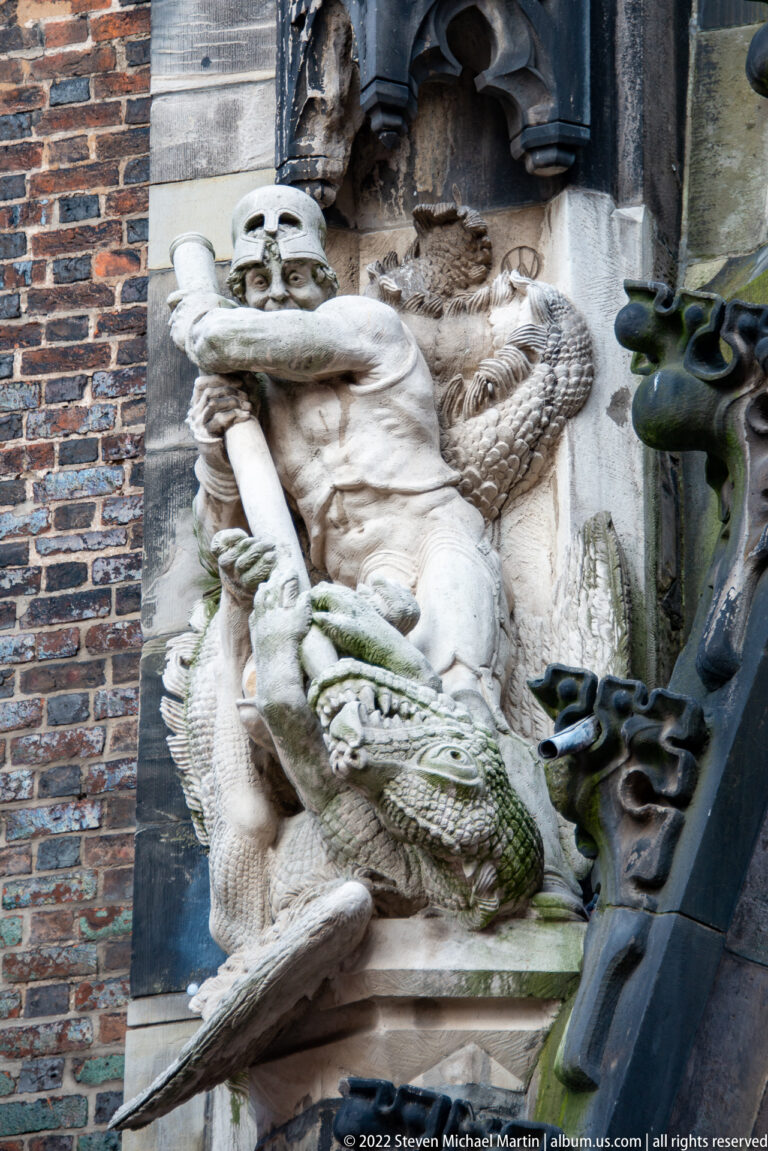 Carved armored figure beside a large scaled dragon-like creature within a weathered architectural setting.
