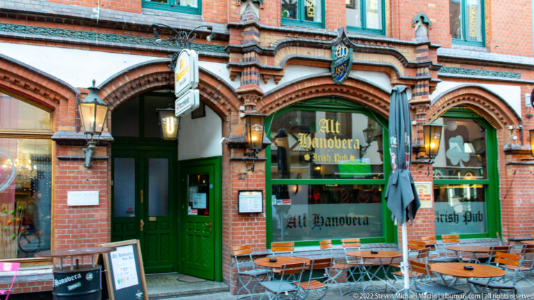 Alt Hannover restaurant with green doors, arched red-brick façade, window lettering, lanterns, and outdoor tables.