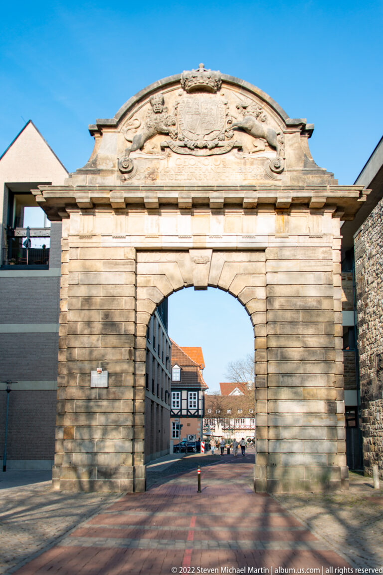Marstalltor stone gateway with a broad central arch and carved heraldic crest, framing old-town buildings beyond.